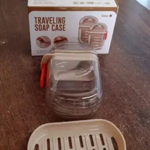 Travel soap case and drain tray shown next to their retail packaging box on a wood table
