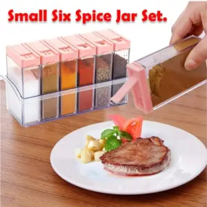 Six spice jars with pink flip-top lids in a clear tray, one jar being used to sprinkle spice onto a plated steak