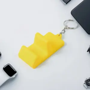 Yellow phone stand keychain on a desk next to a smartwatch and phone