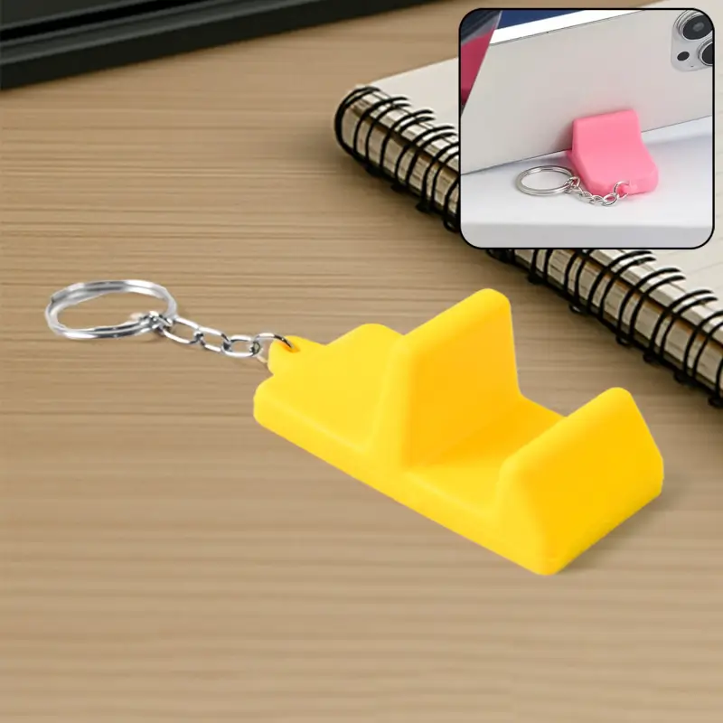 Yellow phone stand keychain on a desk, with an inset showing the pink version propping up a phone