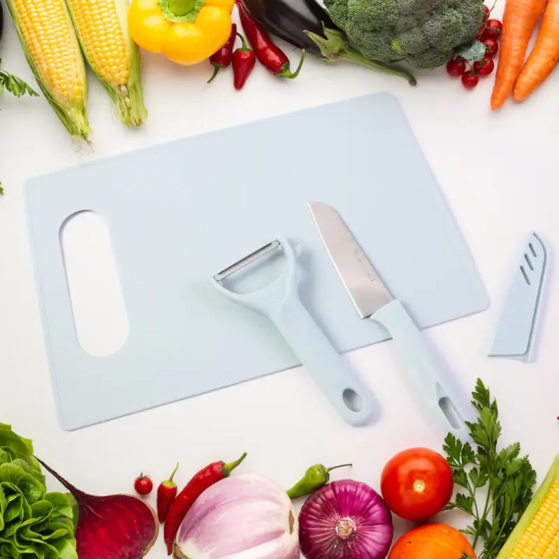 Chopping board, knife and peeler arranged on a table surrounded by fresh vegetables