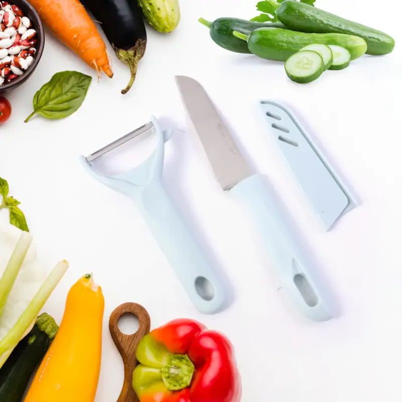 Knife, peeler and blade guard laid out next to fresh vegetables