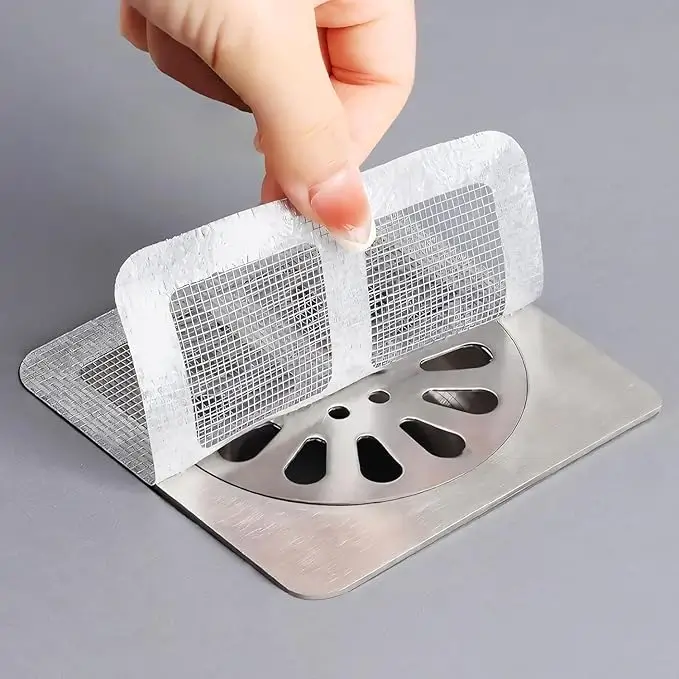 Hand applying a white mesh drain sticker over a metal floor drain grate