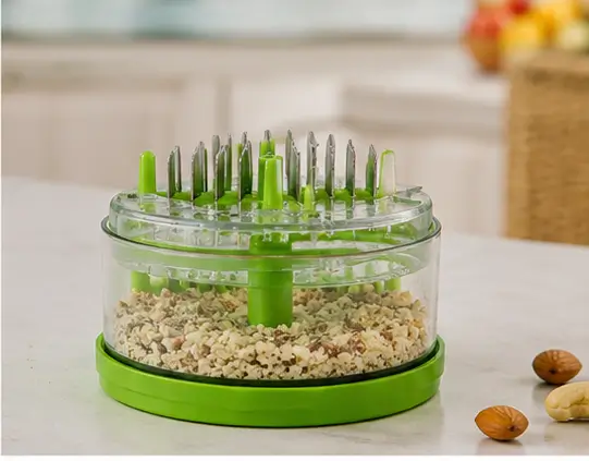 Chopper cup filled with crushed nuts, next to its lid with almonds and cashews on a marble counter